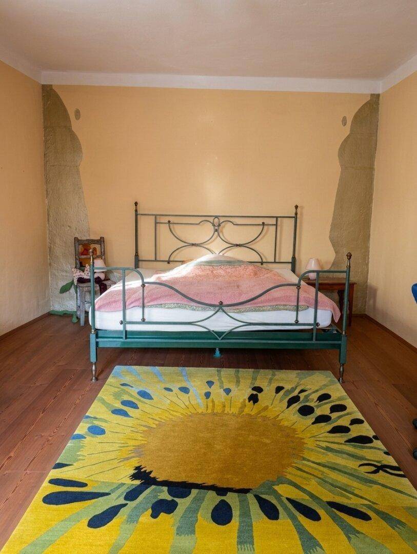 Schlafzimmer mit schmiedeeisernem Bett, Holzboden und einem farbenfrohen Teppich.