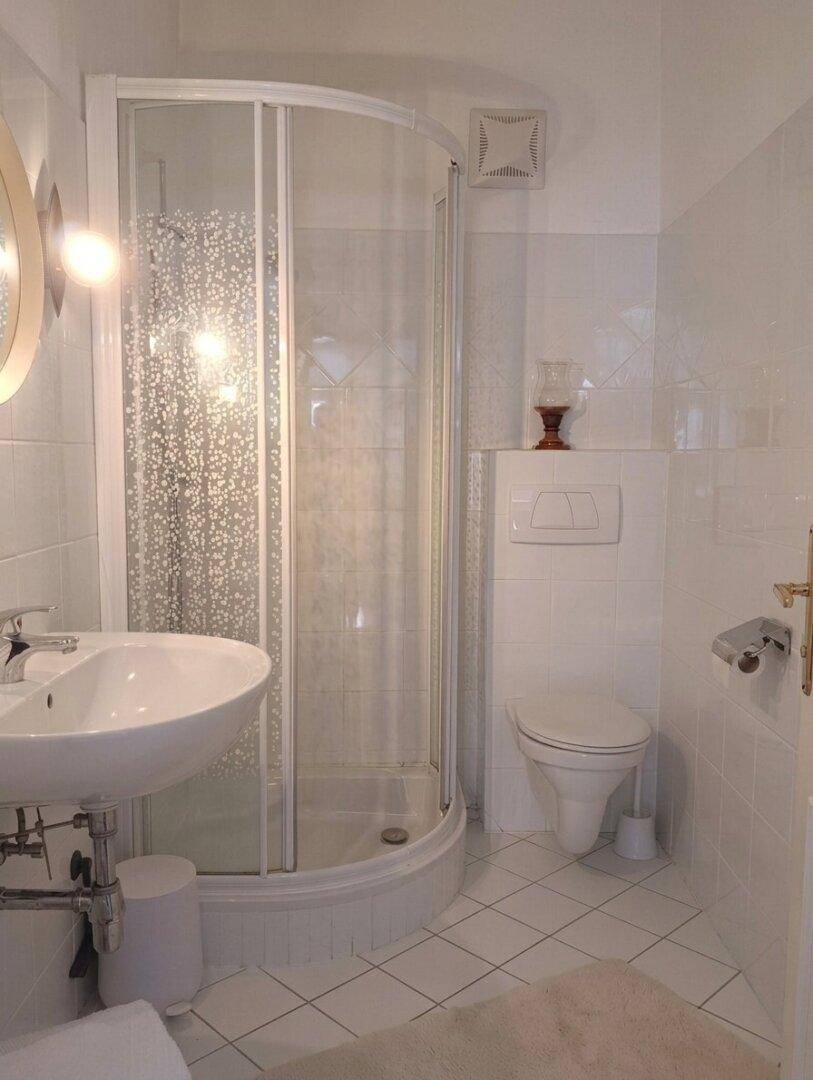 Kleines, hell gefliestes Badezimmer mit Duschkabine, WC und Waschbecken.