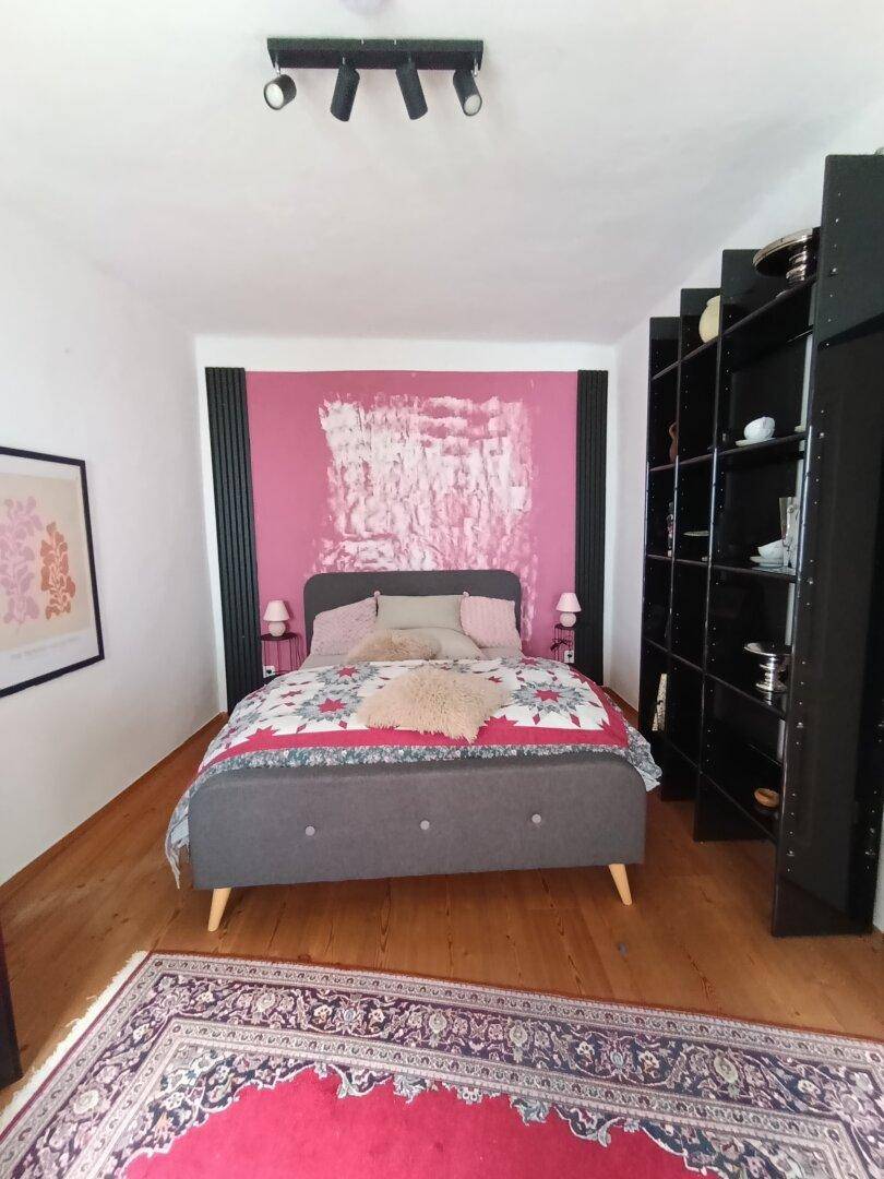 Modernes Schlafzimmer mit pinker Akzentwand, Holzboden und schwarzen Regalen.
