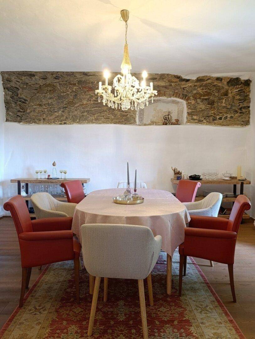 Eleganter Essbereich mit modernem Kronleuchter, freigelegter Steinwand und Holzboden.