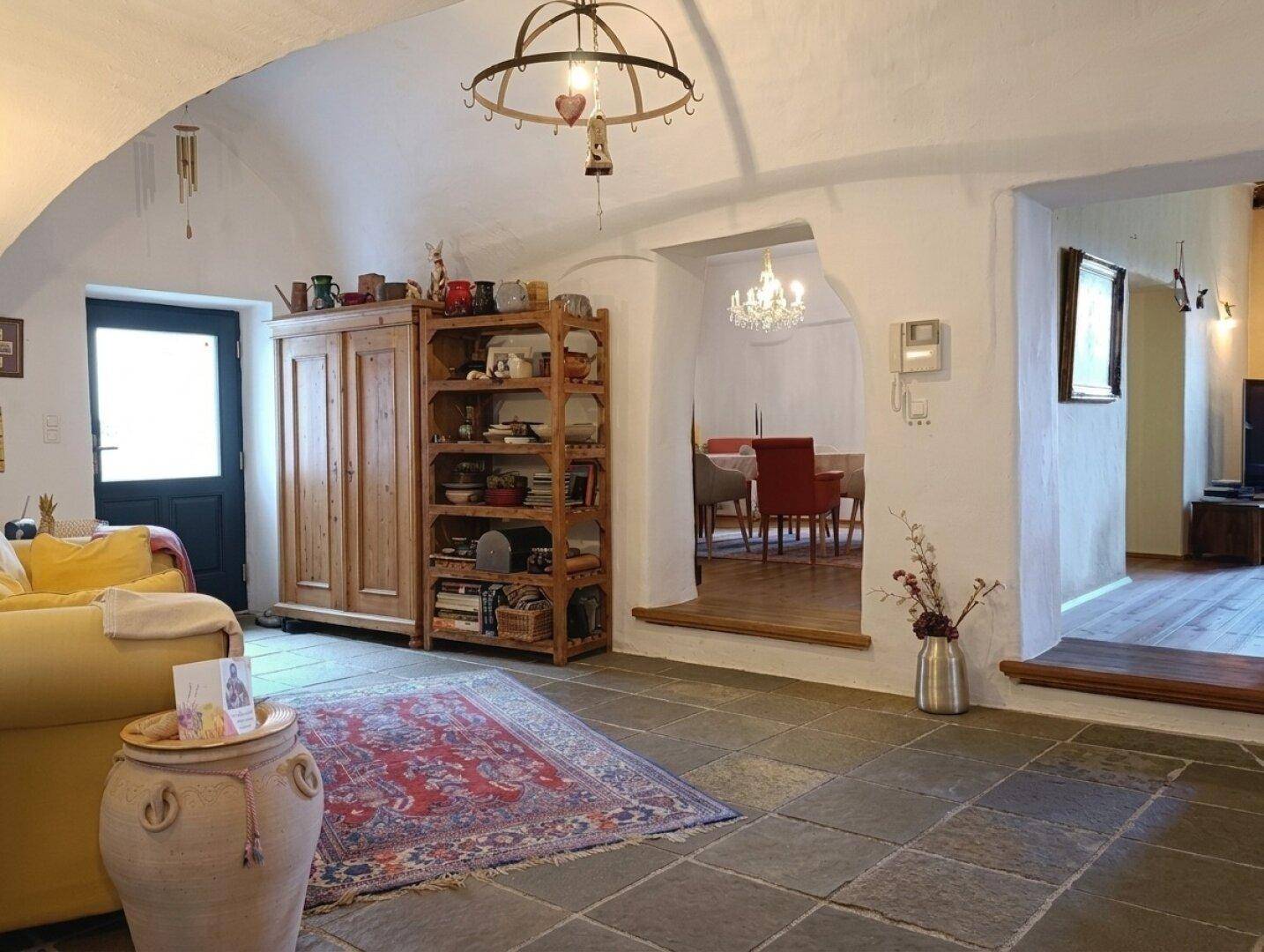 Rustikales Wohnzimmer mit Gewölbedecke, Natursteinboden und Blick in den Essbereich.