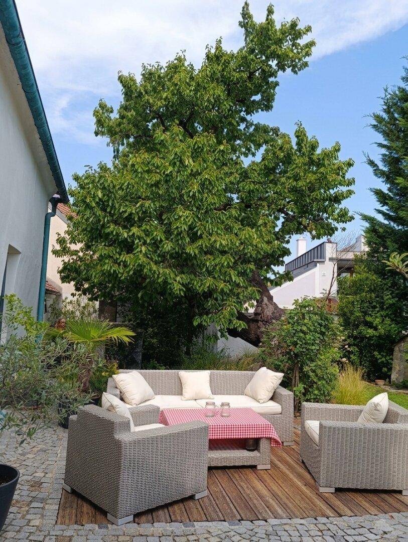 Moderne Terrasse mit bequemen Outdoor-Möbeln auf einem Holzdeck unter einem großen Baum.