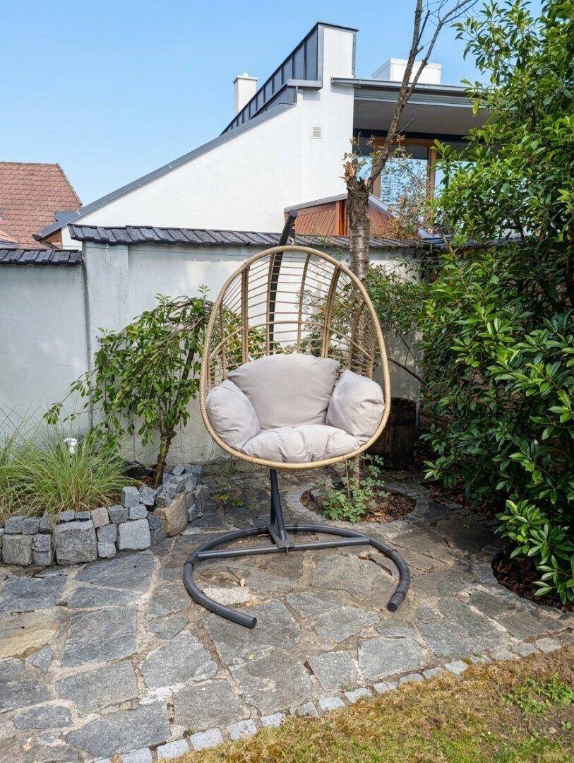 Ruhiger Gartenbereich mit Hängesessel, Natursteinpflaster und grüner Bepflanzung.