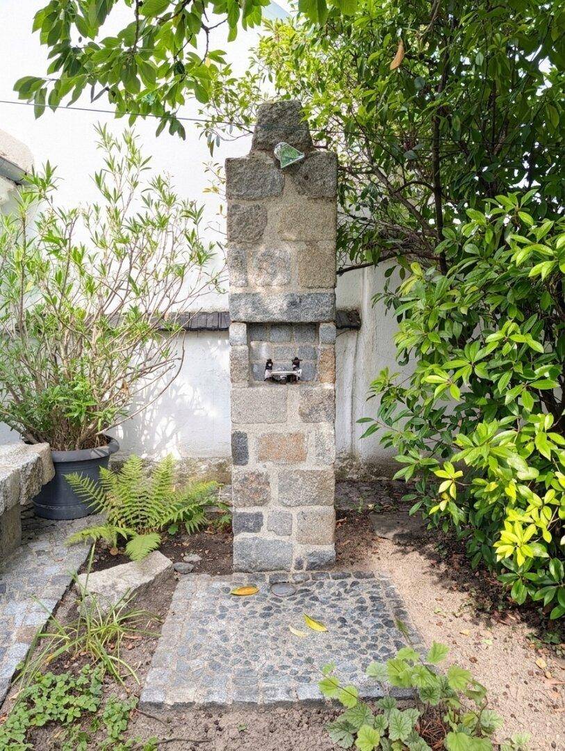 Rustikale Steinsäule im Garten, möglicherweise eine Außendusche oder ein Wasserspiel.