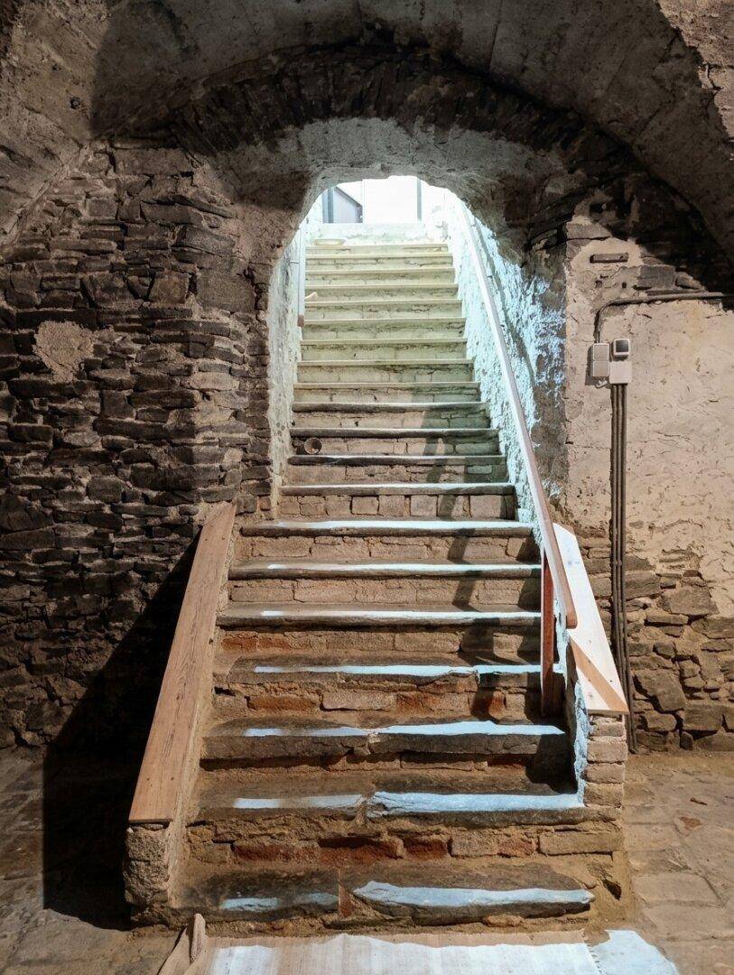 Historische Steintreppe führt hinab in einen gewölbten Kellerraum mit rustikalen Wänden.