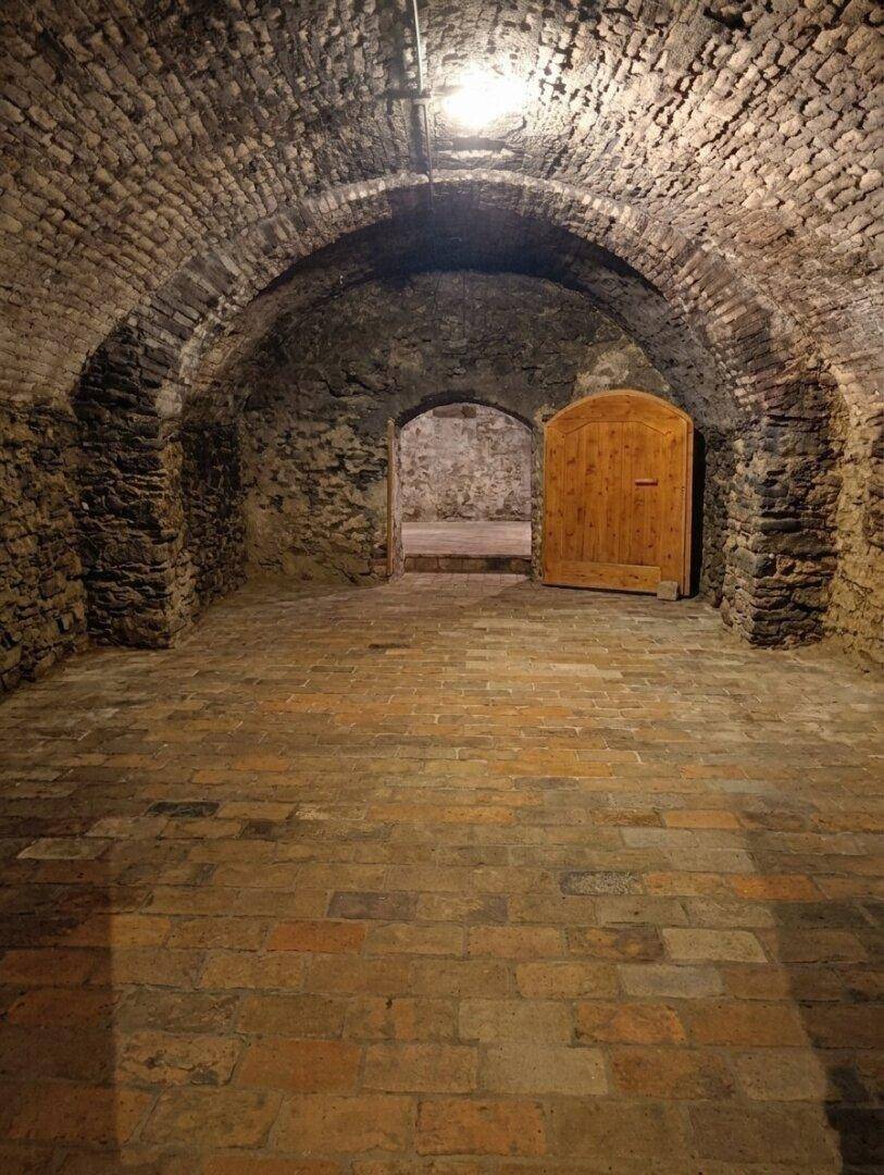 Historischer Gewölbekeller mit Ziegelwänden und -boden, ideal zur Weinlagerung.