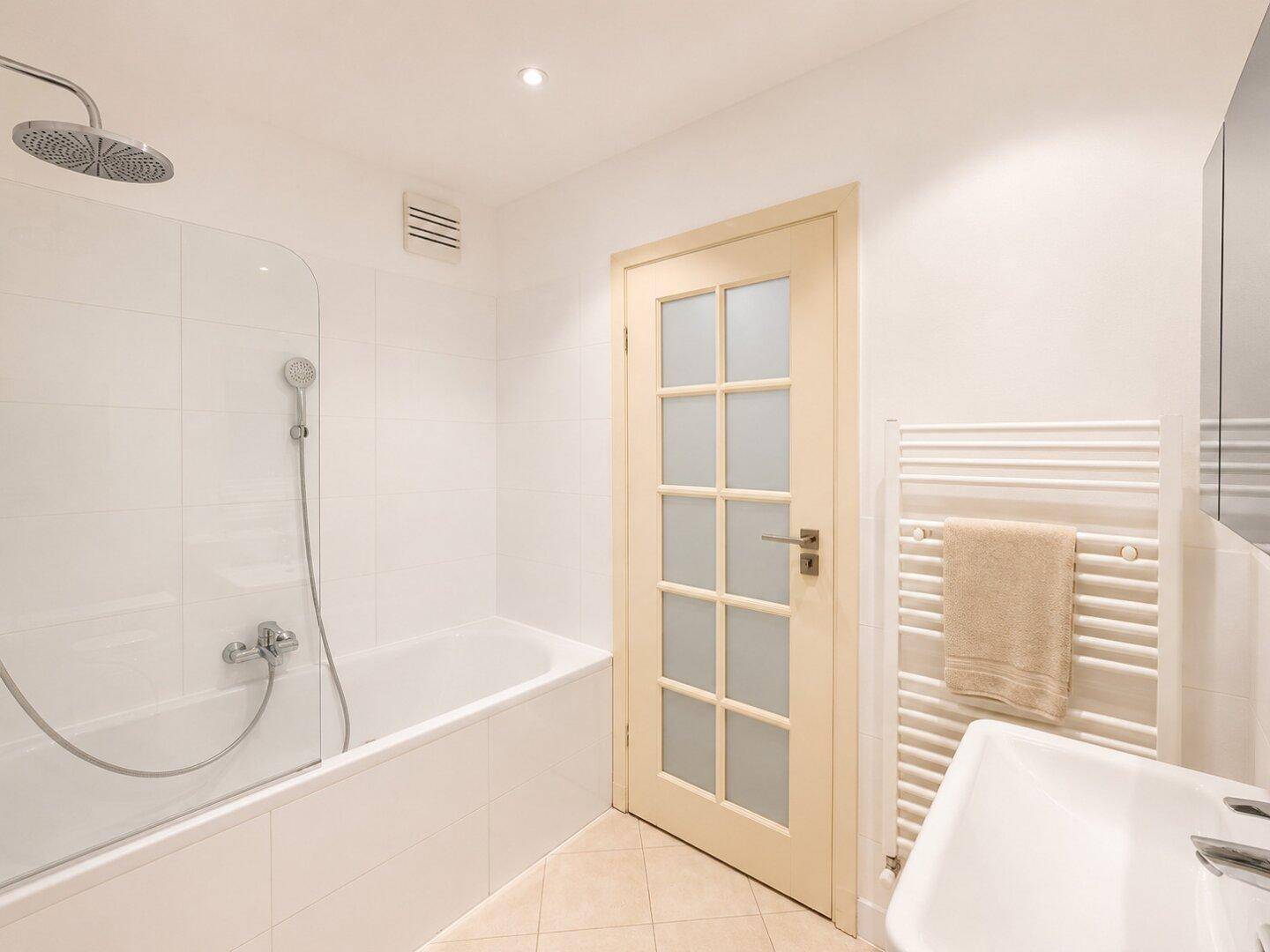Modernes Badezimmer mit Badewanne, Duschfunktion und beheiztem Handtuchhalter.