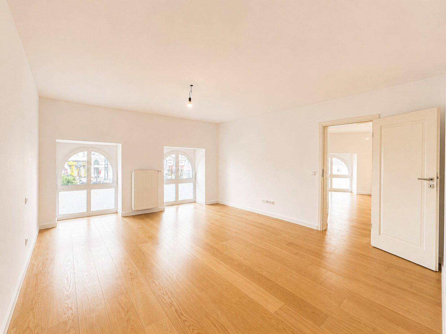 Heller, leerer Raum mit Holzboden und zwei großen Rundbogenfenstern, bereit zur Einrichtung.