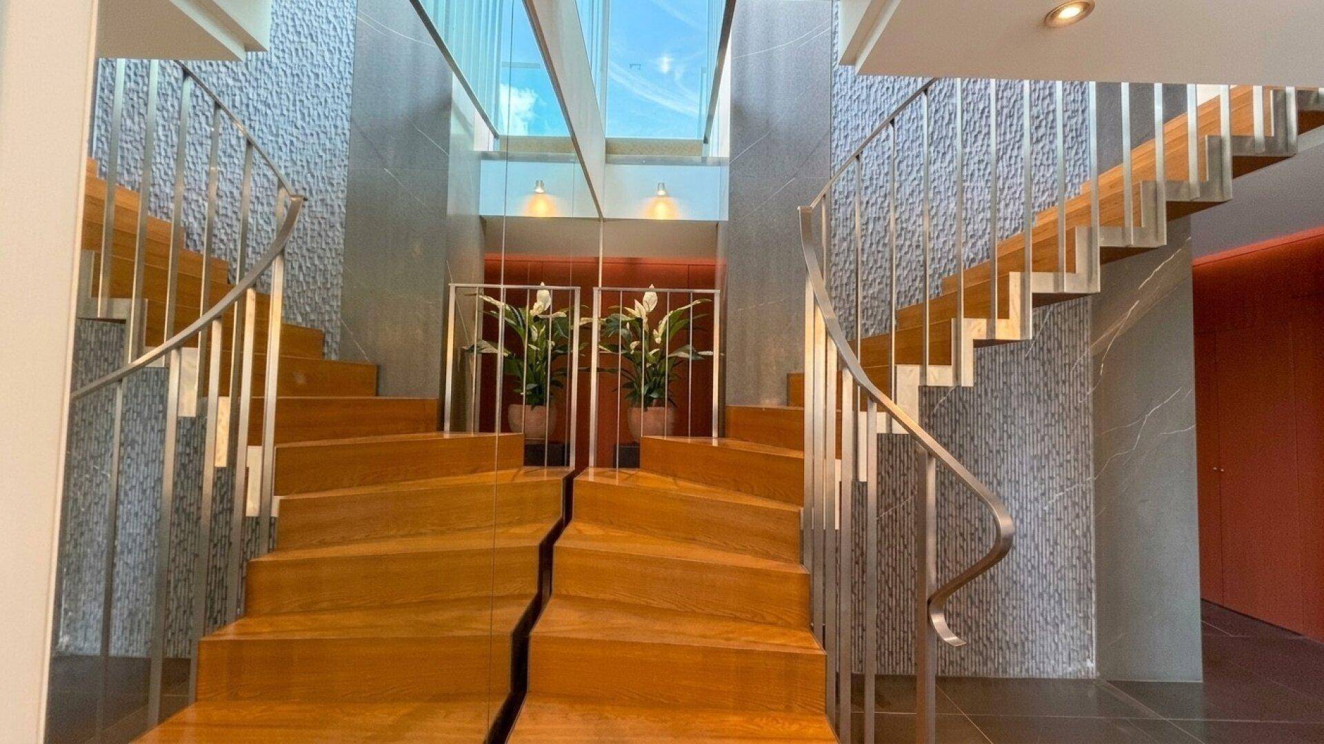 Elegantes Treppenhaus mit Holzstufen, Metallgeländer und Oberlicht für viel Tageslicht.
