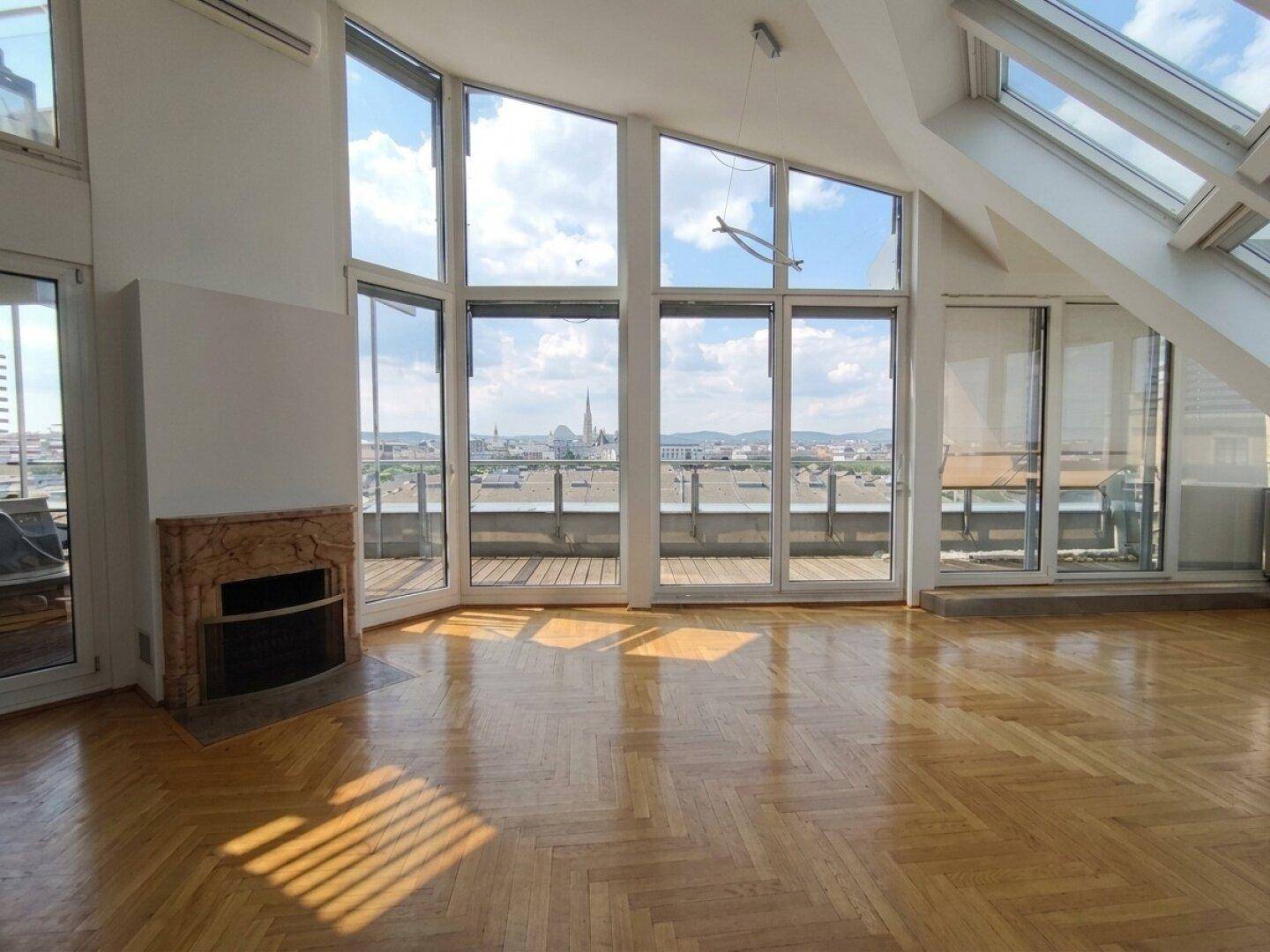 Geräumiges Wohnzimmer mit Fischgrätparkett, Kamin und bodentiefen Fenstern mit Stadtblick.