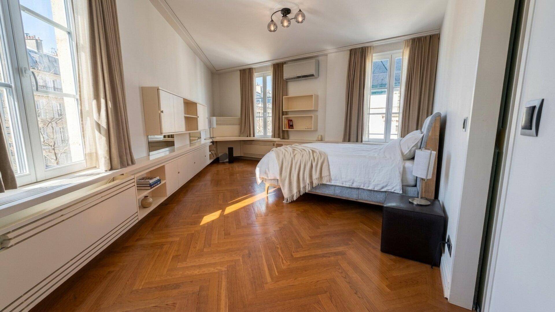 Helles Schlafzimmer mit Fischgrätparkett, großen Fenstern und integrierten Möbeln.
