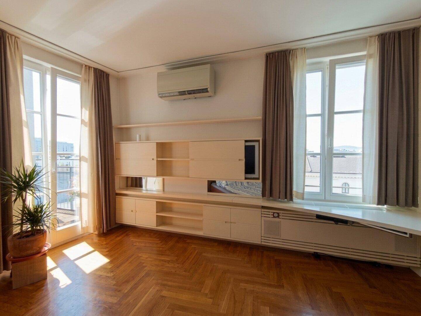 Heller Raum mit Fischgrätparkett, Einbauschränken und Zugang zu einem Balkon.