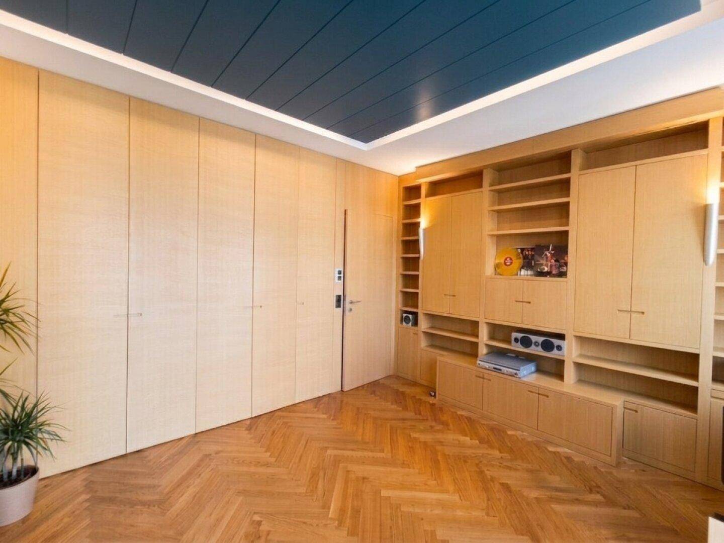 Raum mit maßgefertigten Holzschränken, Fischgrätparkett und indirekter Deckenbeleuchtung.