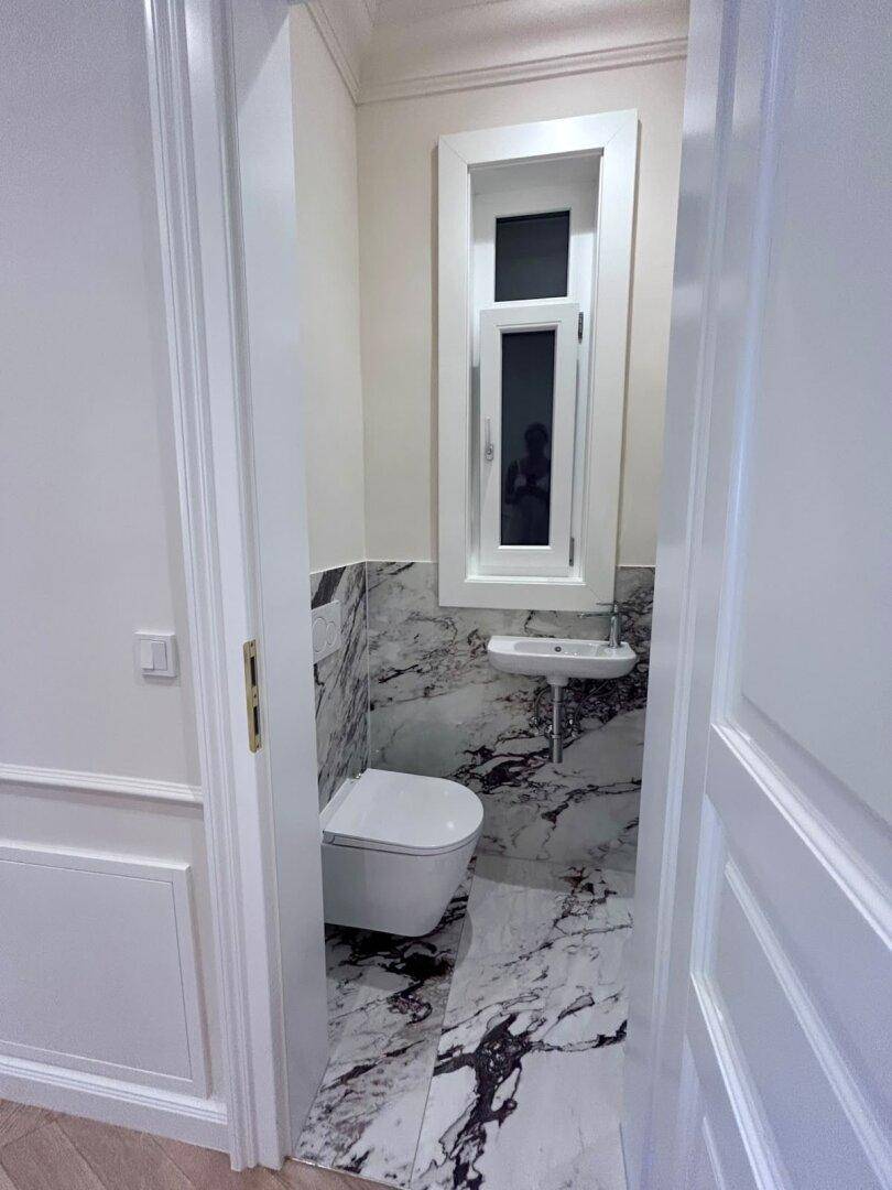 Modernes Gäste-WC mit Marmorfliesen, wandhängender Toilette und einem schmalen Fenster für Belüftung.