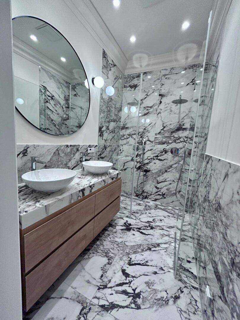Luxuriöses Badezimmer mit Marmorfliesen, Doppelwaschbecken und einer geräumigen begehbaren Dusche.