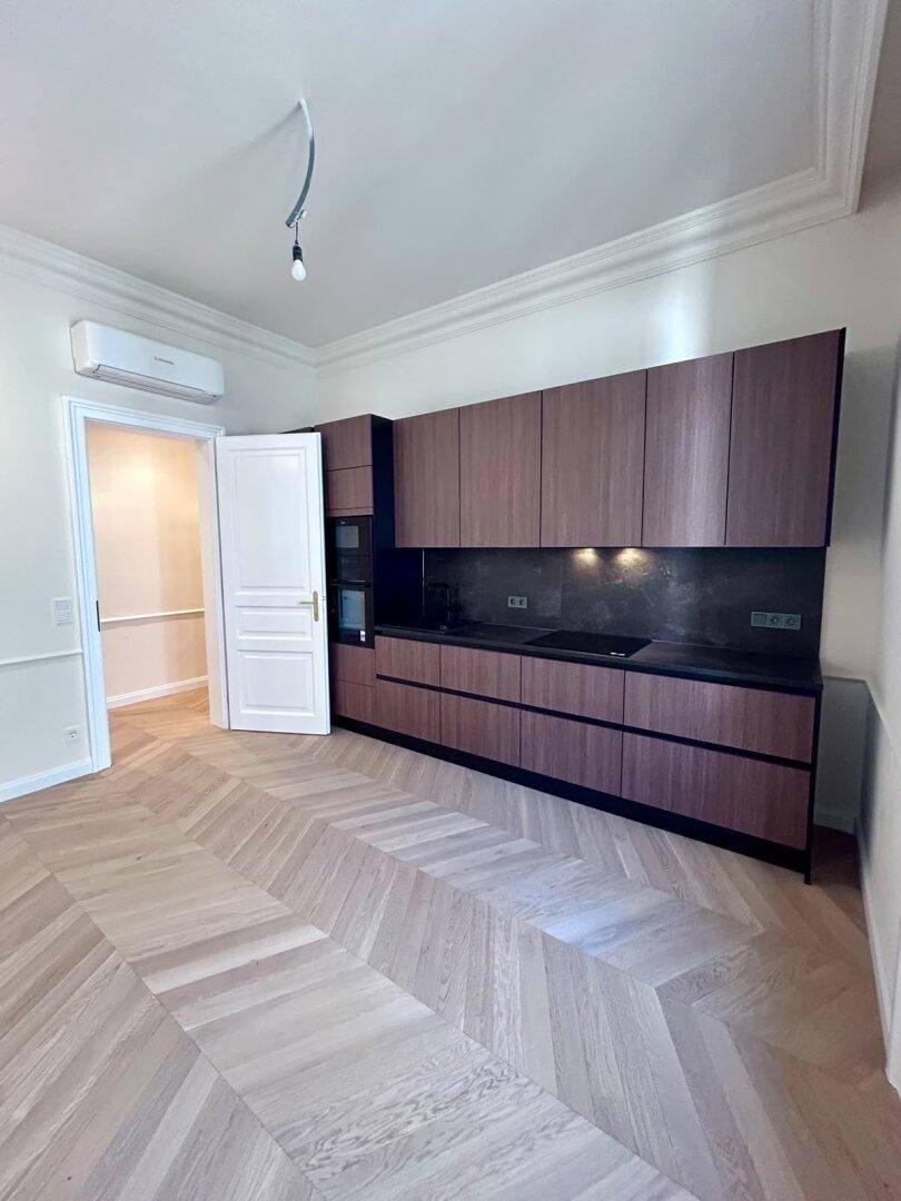 Moderne Einbauküche mit dunklen Holzfronten und integrierten Geräten in einem hellen Raum mit Parkettboden.