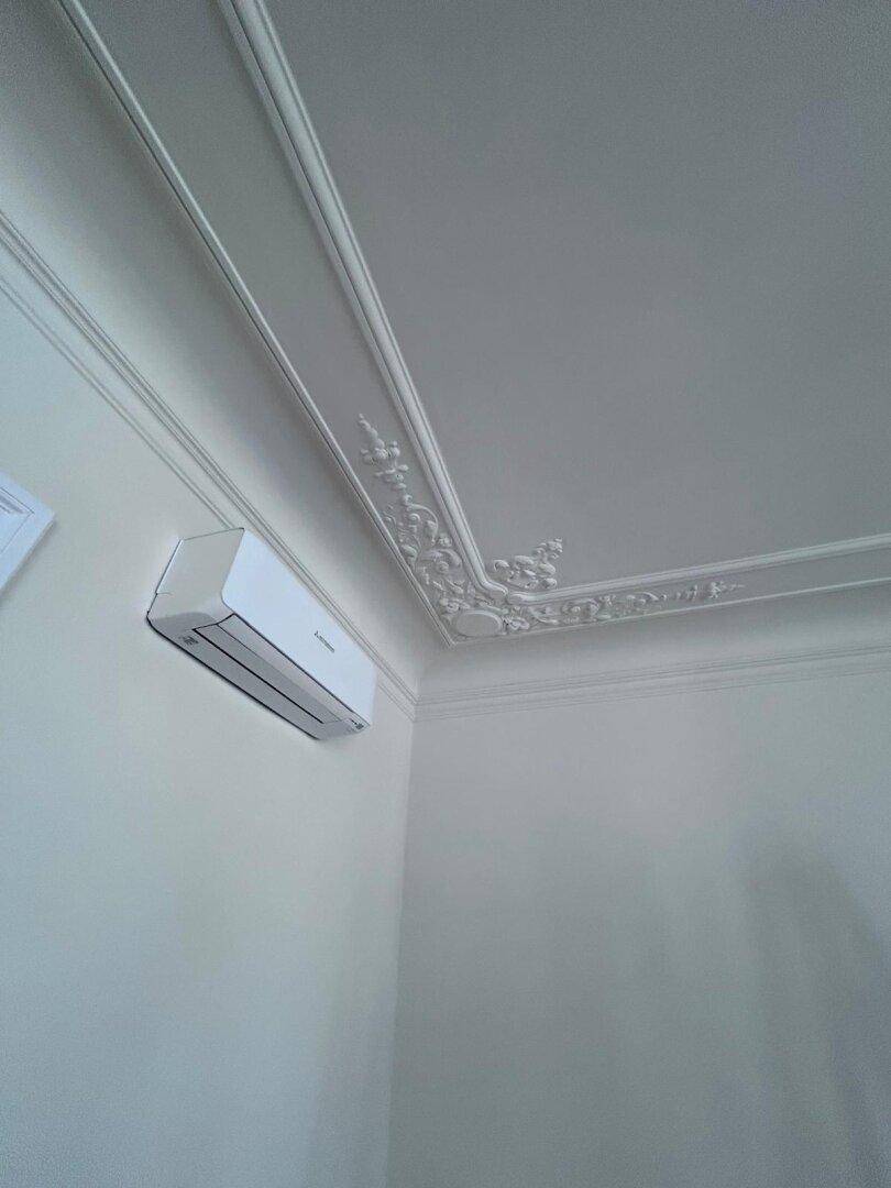 Detailaufnahme einer Stuckdecke mit integrierter Klimaanlage in einem hellen Raum.