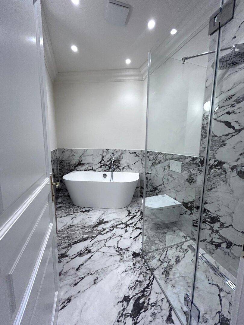 Elegantes Badezimmer mit freistehender Badewanne, Marmorfliesen und einer modernen Glasdusche.