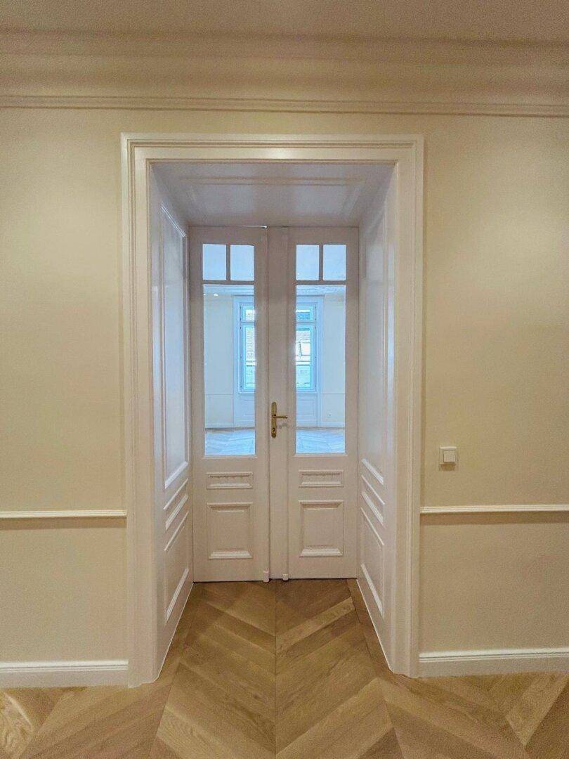 Elegante Doppeltüren mit Glaseinsätzen in einem hellen Flur mit Fischgrätparkett.
