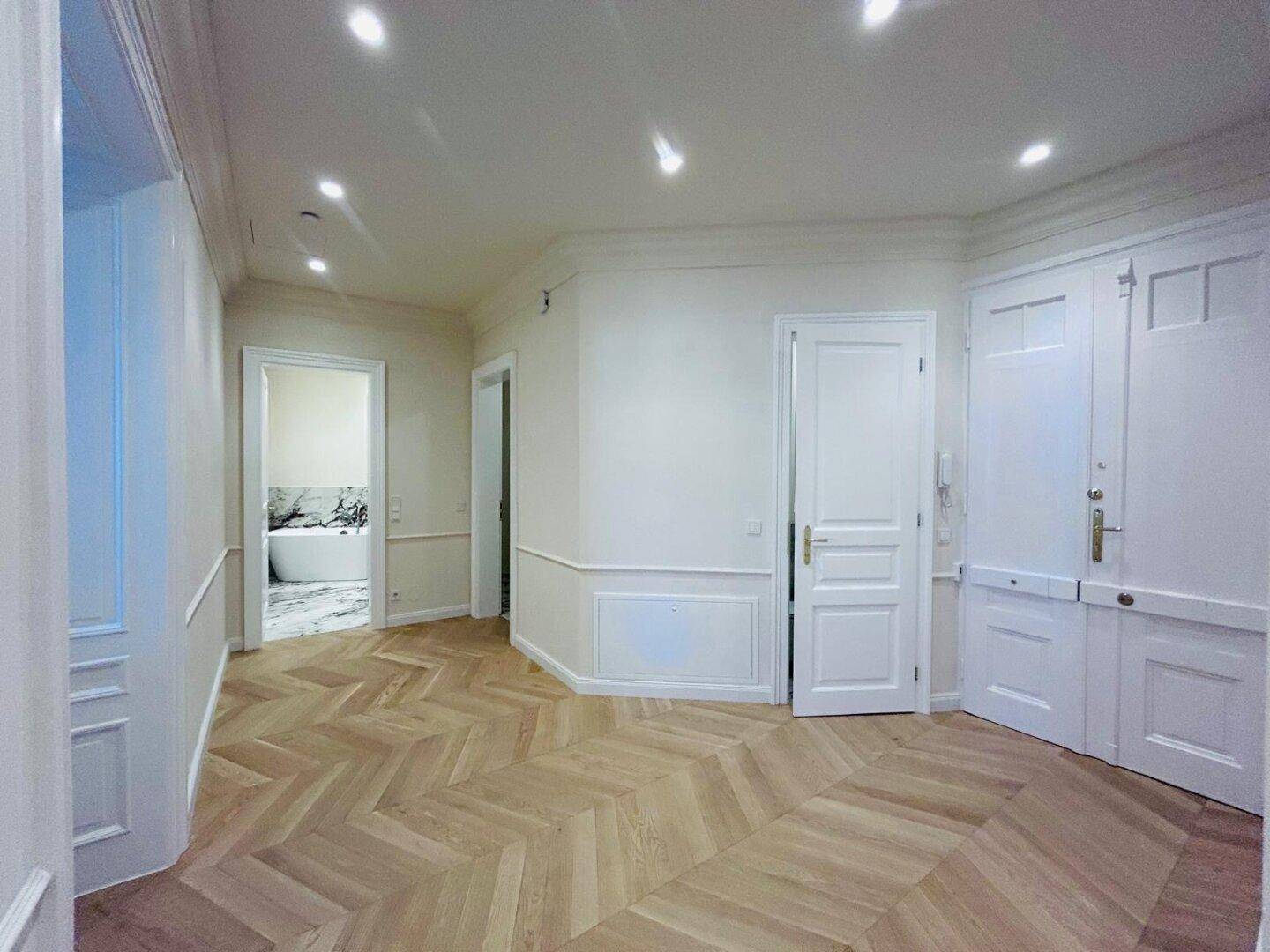 Eleganter Flur mit Fischgrätparkett, Einbauschränken und Zugang zu einem modernen Badezimmer.