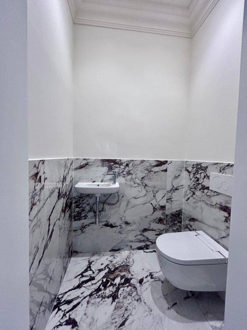 Stilvolles Gäste-WC mit Marmorfliesen, wandhängender Toilette und minimalistischem Waschbecken.