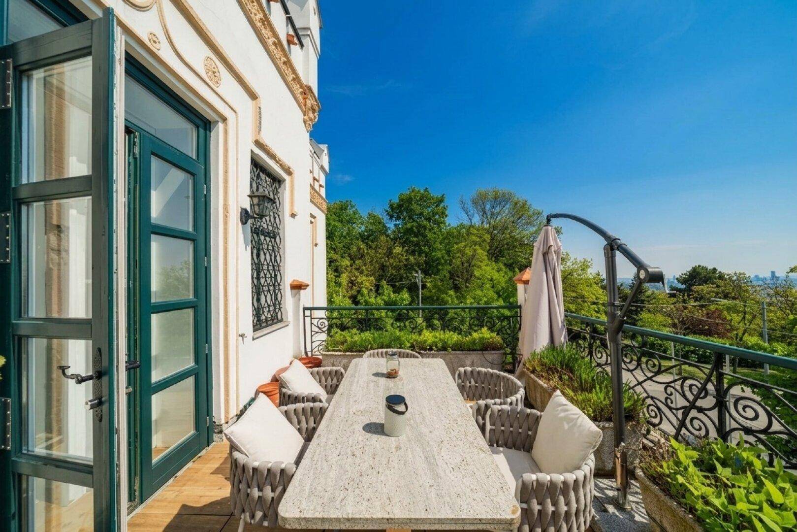 Gemütlicher Balkon mit Esstisch und Stühlen, bietet einen malerischen Blick auf die grüne Umgebung und die Stadt.