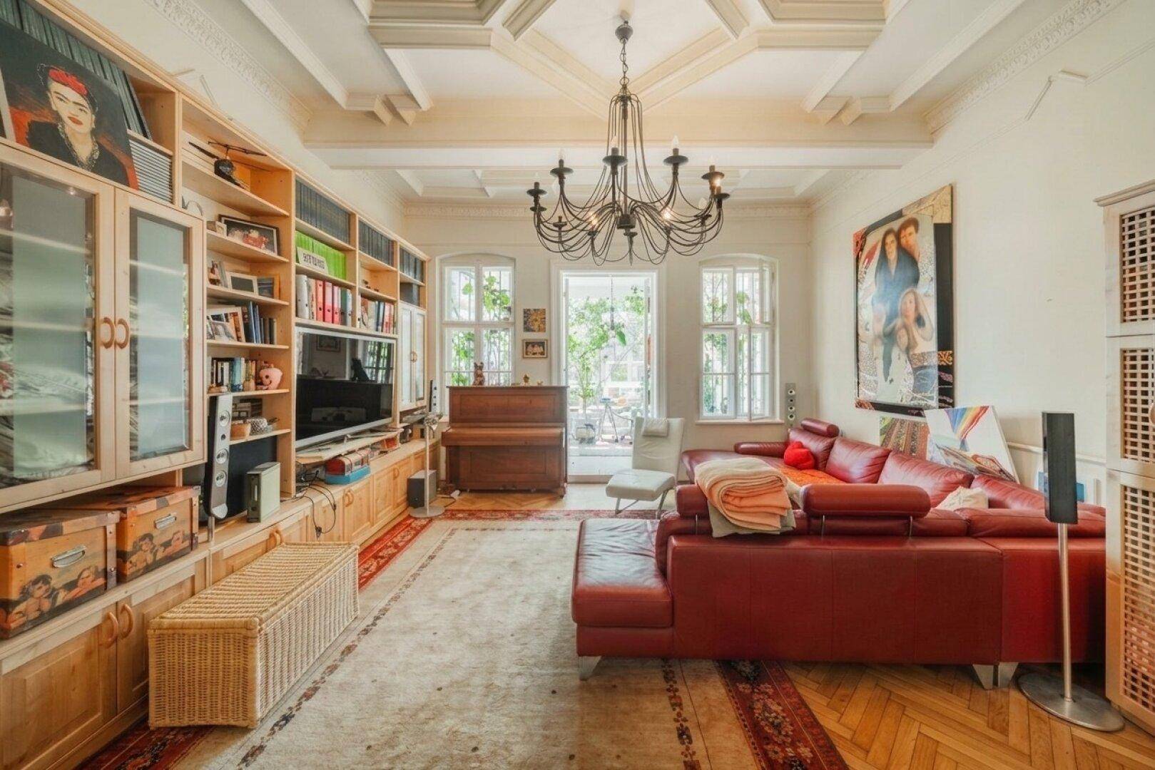 Geräumiges Wohnzimmer mit rotem Ledersofa, Bücherregalen und einer eleganten Kassettendecke.