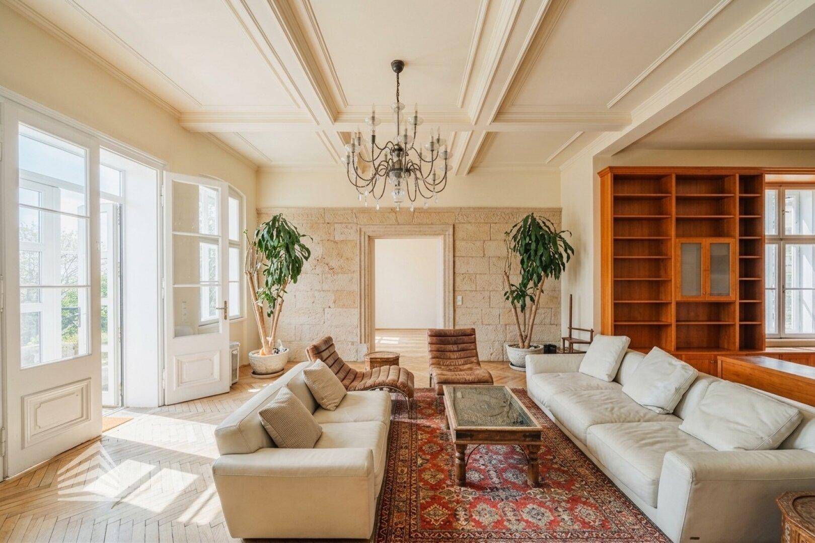 Großzügiges Wohnzimmer mit hellen Sofas, hohen Decken und großen Fenstertüren, die nach draußen führen.