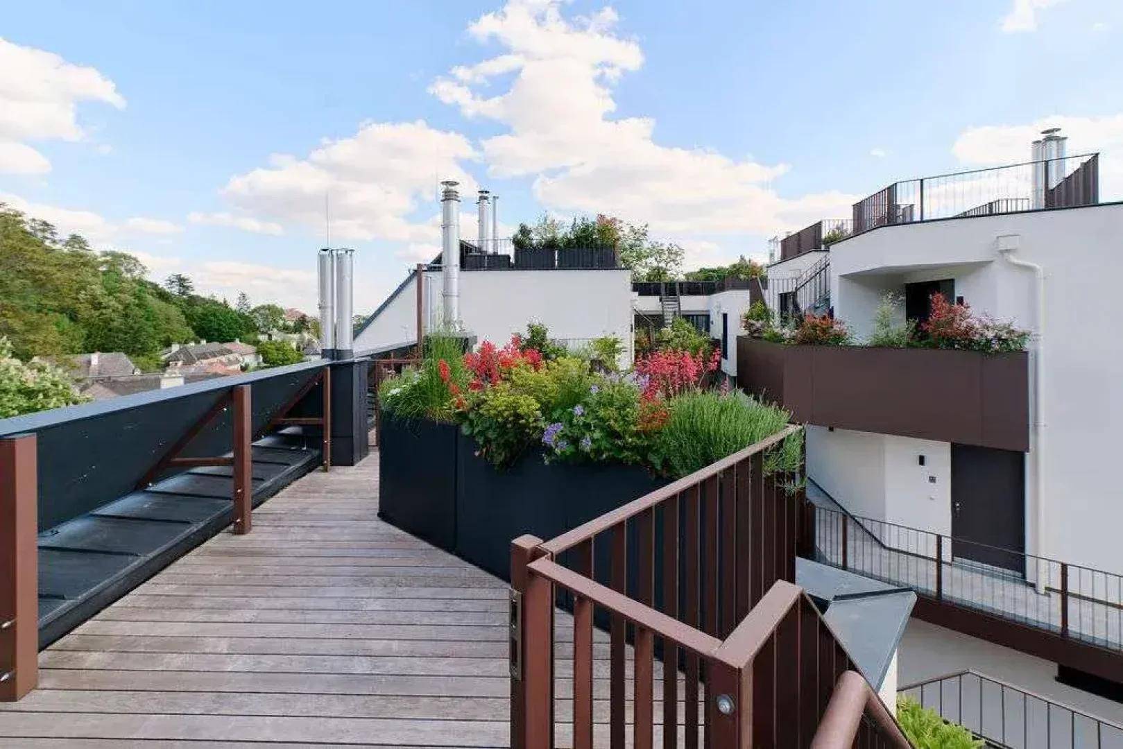 Weitläufige Dachterrasse mit Holzbelag, Pflanzenkübeln und Blick auf moderne Architektur.