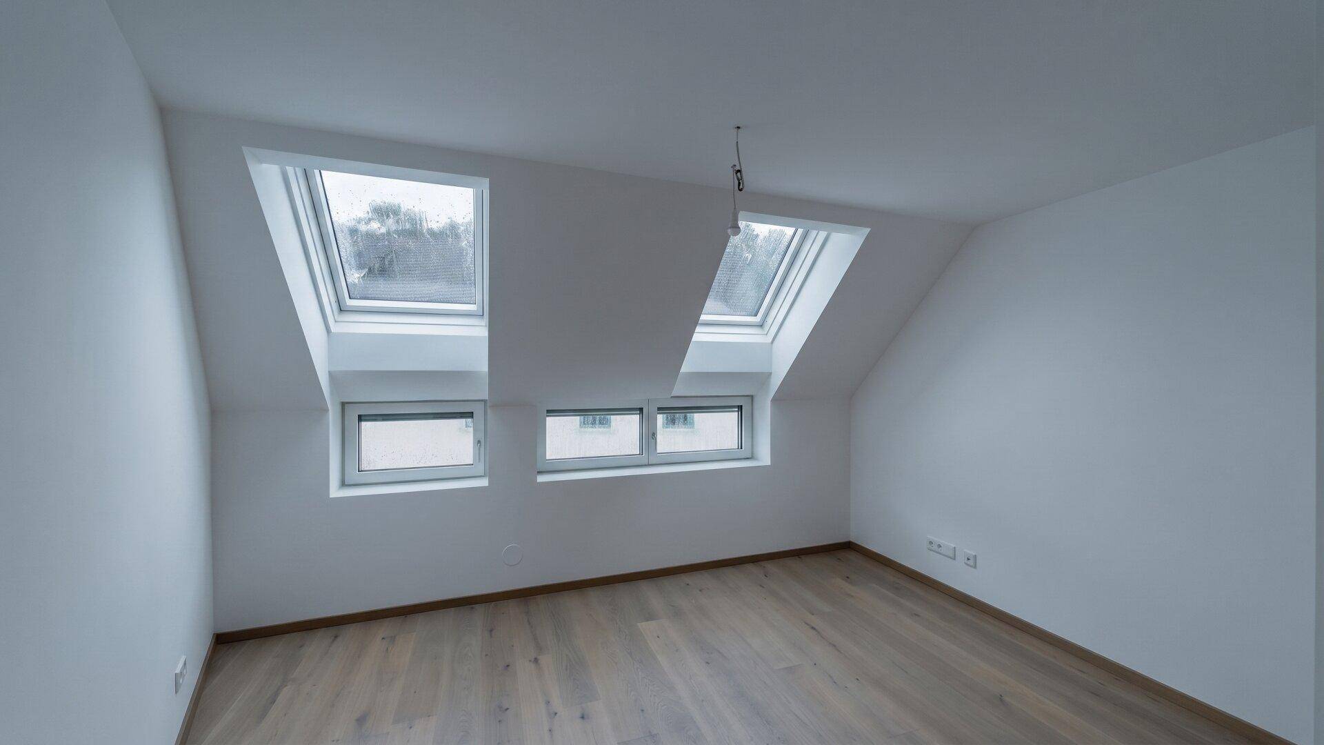 Leeres Dachgeschosszimmer mit schrägen Wänden, Dachfenstern und hellem Holzparkettboden.