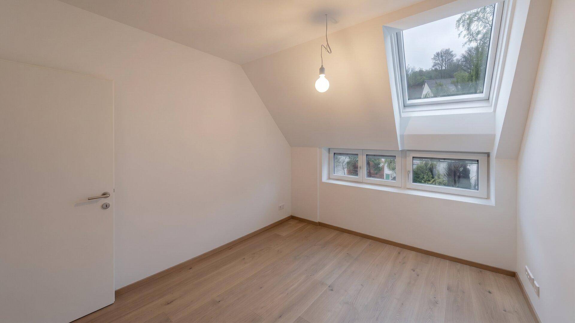 Helles, unmöbliertes Zimmer im Dachgeschoss mit Dachfenstern und Holzboden.