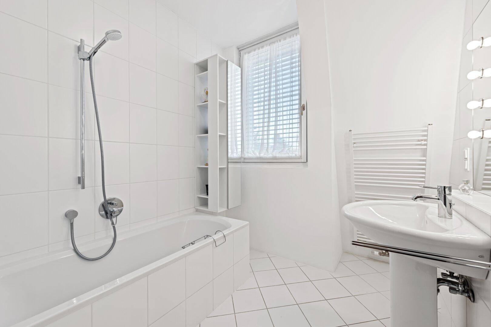 Helles Badezimmer mit Badewanne, Dusche, Waschbecken und Fenster, komplett gefliest.