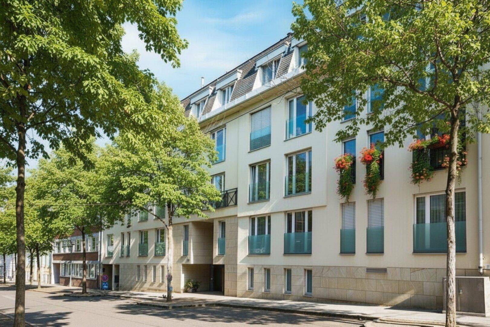 Moderne Wohnhausfassade mit vielen Fenstern und Balkonen, umgeben von Bäumen.