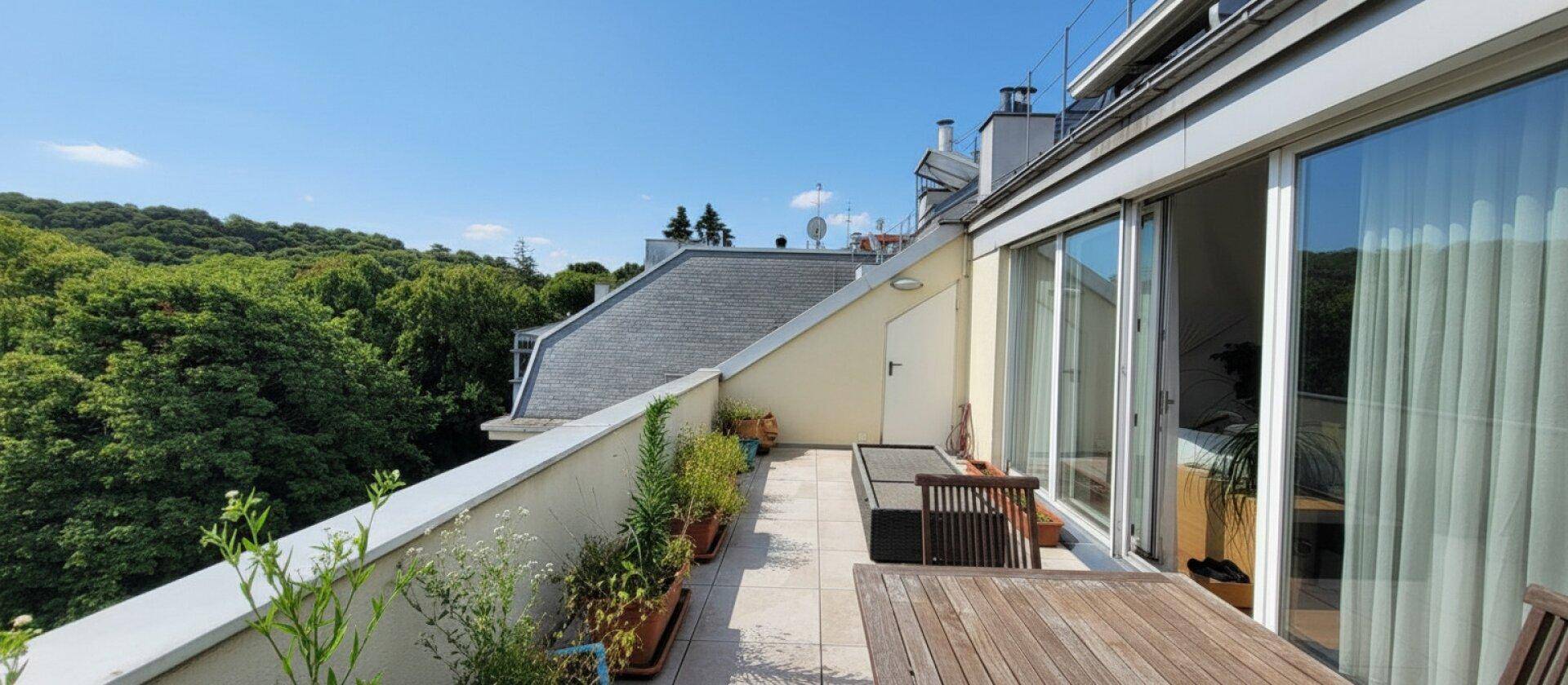 Weitläufige Dachterrasse mit Holztisch und Pflanzen, umgeben von viel Grün.