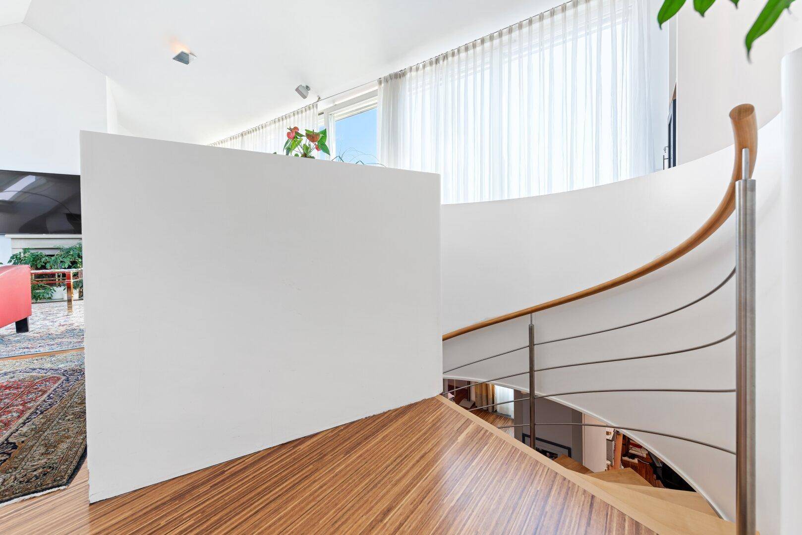 Elegante Treppe mit Holzgeländer und Blick in den offenen Wohnbereich, lichtdurchflutet.