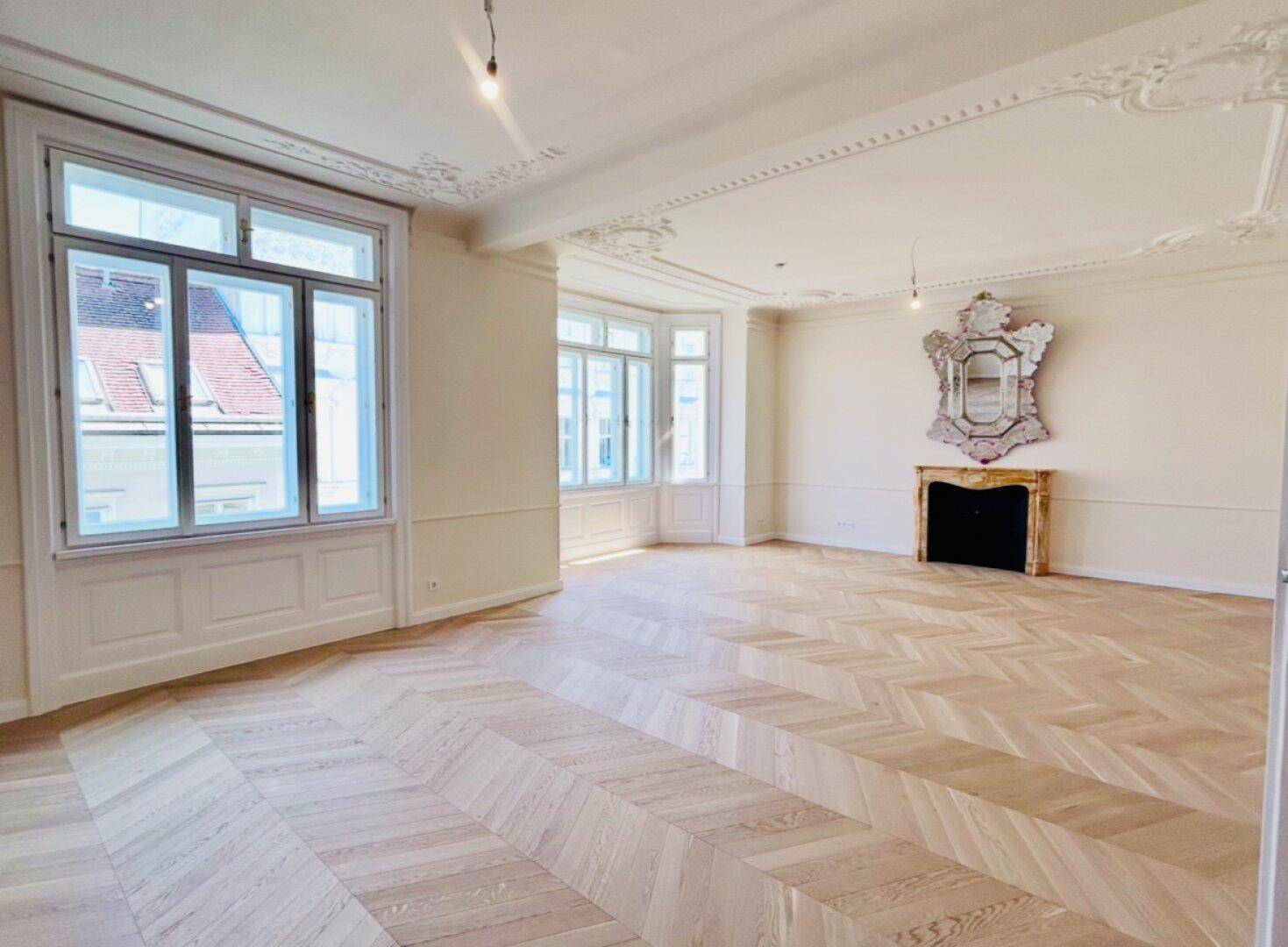 Helles Wohnzimmer mit elegantem Fischgrätparkett, hohen Decken und klassischem Kamin in einem Altbau.