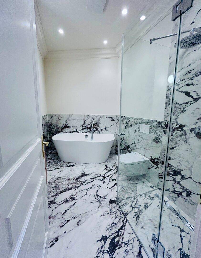 Elegantes Badezimmer mit freistehender Badewanne, Marmorfliesen und einer modernen Glasdusche.
