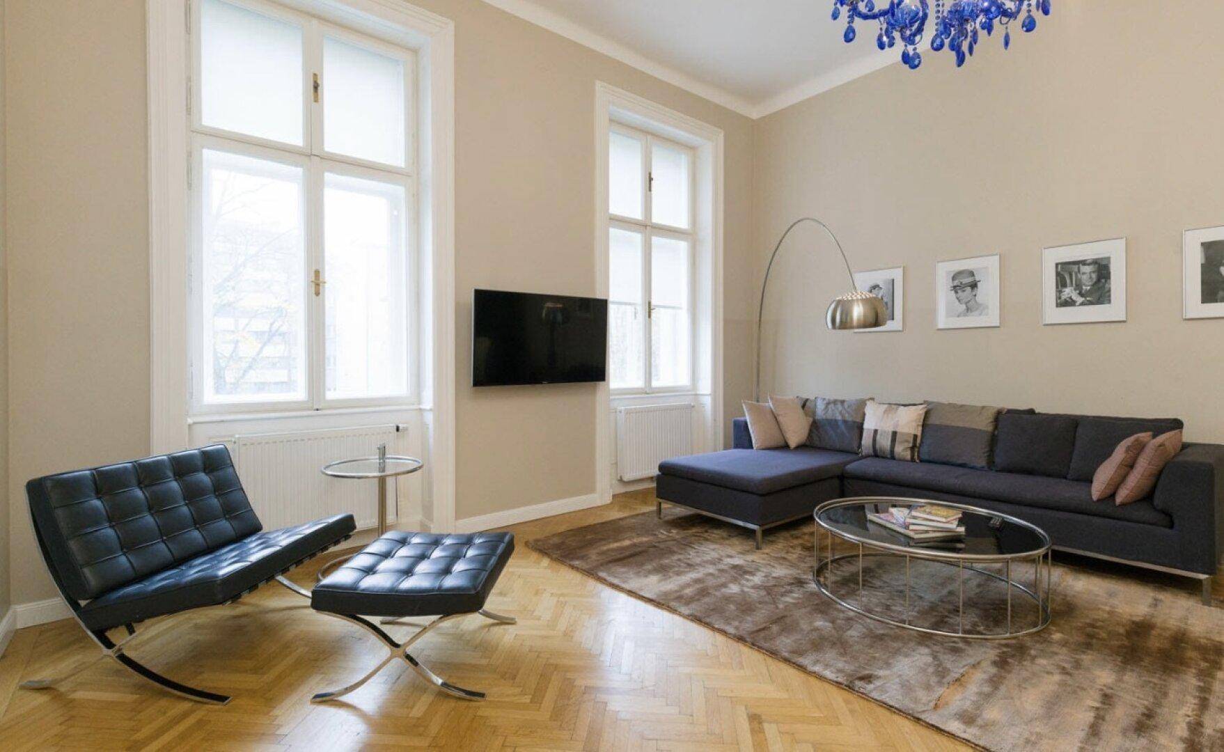 Helles Wohnzimmer mit Fischgrätparkett, modernem Sofa und einem auffälligen blauen Kronleuchter.