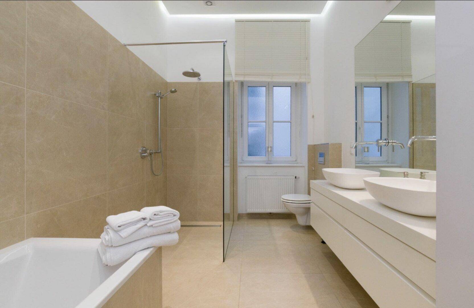 Modernes Badezimmer mit beigen Fliesen, begehbarer Dusche, Doppelwaschbecken und Badewanne.
