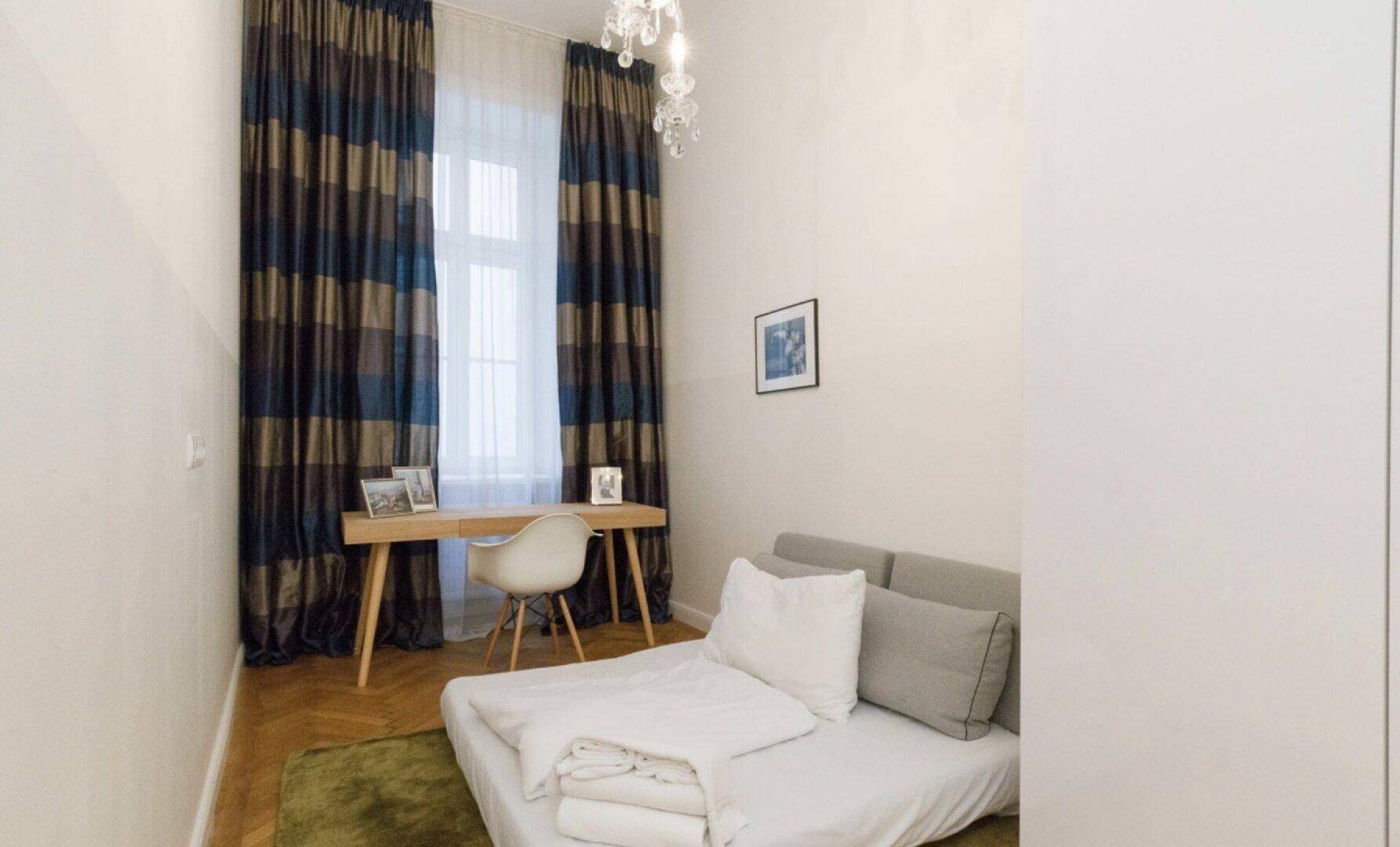Gemütliches Schlafzimmer mit Schreibtisch, Fischgrätparkett und farbigen Vorhängen.
