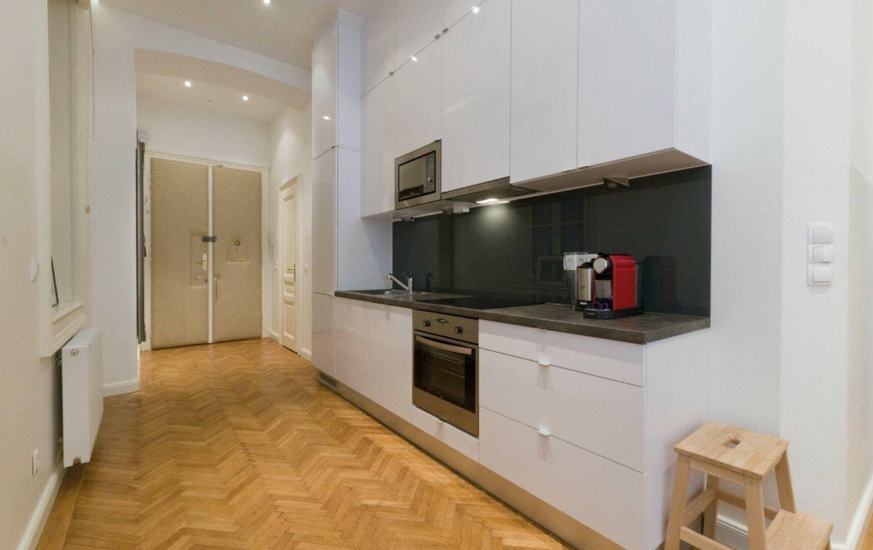 Moderne Küchenzeile in Weiß mit integrierten Geräten und Holzboden im Flur.