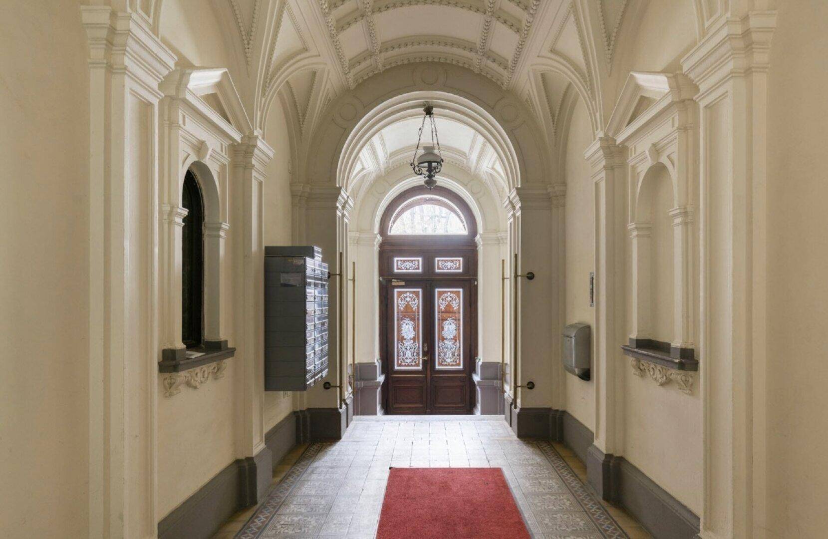 Historischer Eingangsbereich mit hohen Gewölbedecken, verzierten Wänden und einer eleganten Holztür.