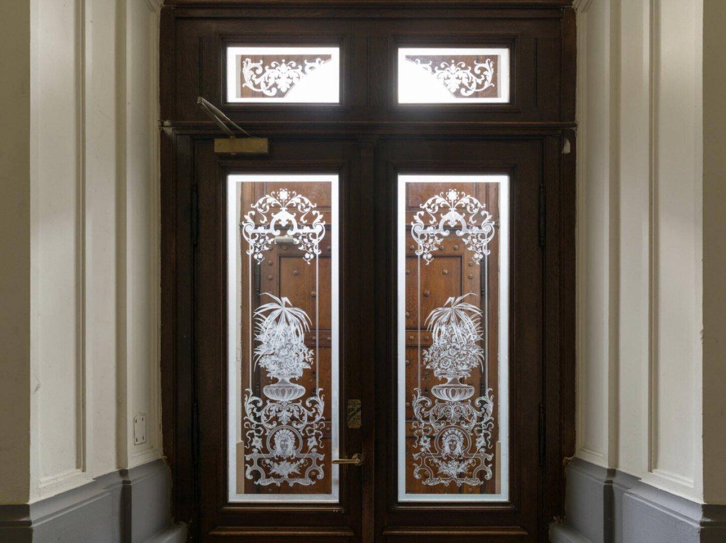 Detailaufnahme einer kunstvoll verzierten Eingangstür mit geätztem Glas und Holzelementen im Flur.