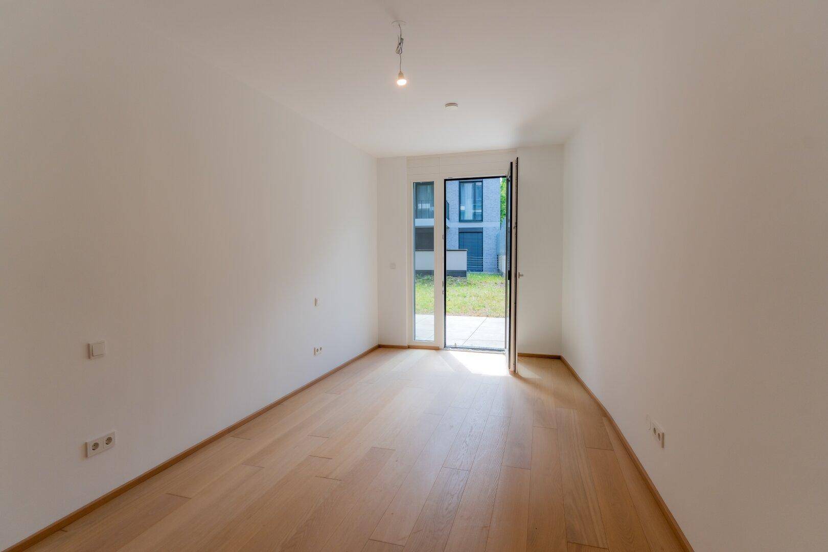 Lichtdurchfluteter Raum mit hellem Holzboden und direktem Zugang zur Außenterrasse.