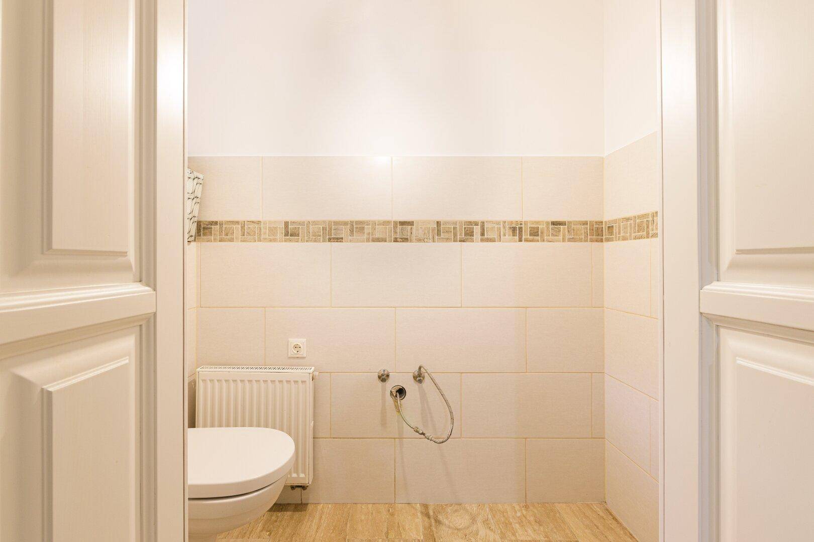 Separates WC mit Wandfliesen, Heizkörper und einfacher Toilette, durch Türrahmen sichtbar.