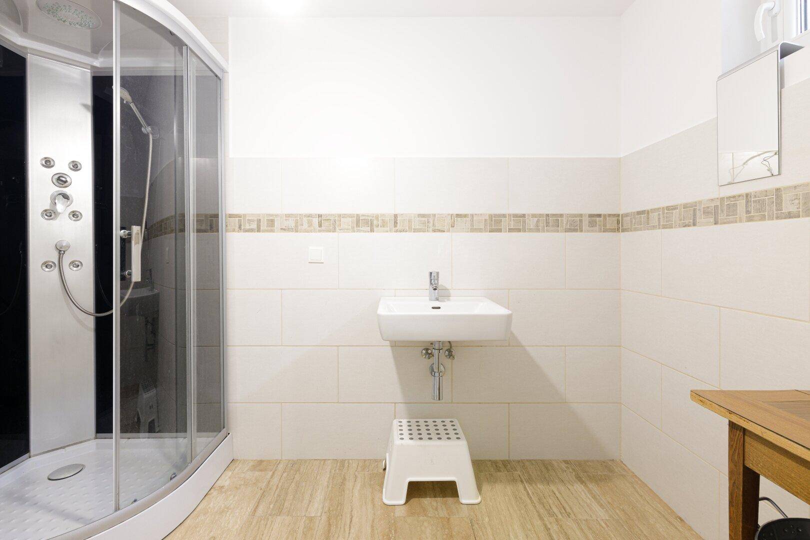 Modernes Badezimmer mit Duschkabine, Waschbecken und hellen Fliesen an den Wänden.