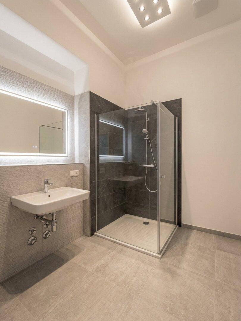Modernes Badezimmer mit begehbarer Dusche, Einzelwaschbecken und beleuchtetem Spiegel.