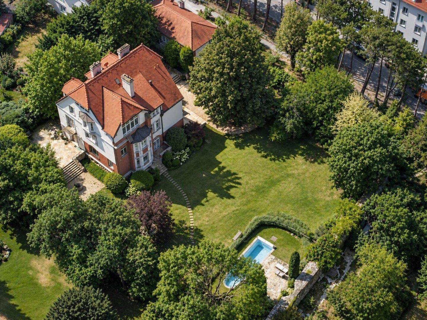 Luftaufnahme einer weitläufigen Villa mit großem Garten, Pool und umgebender grüner Landschaft.