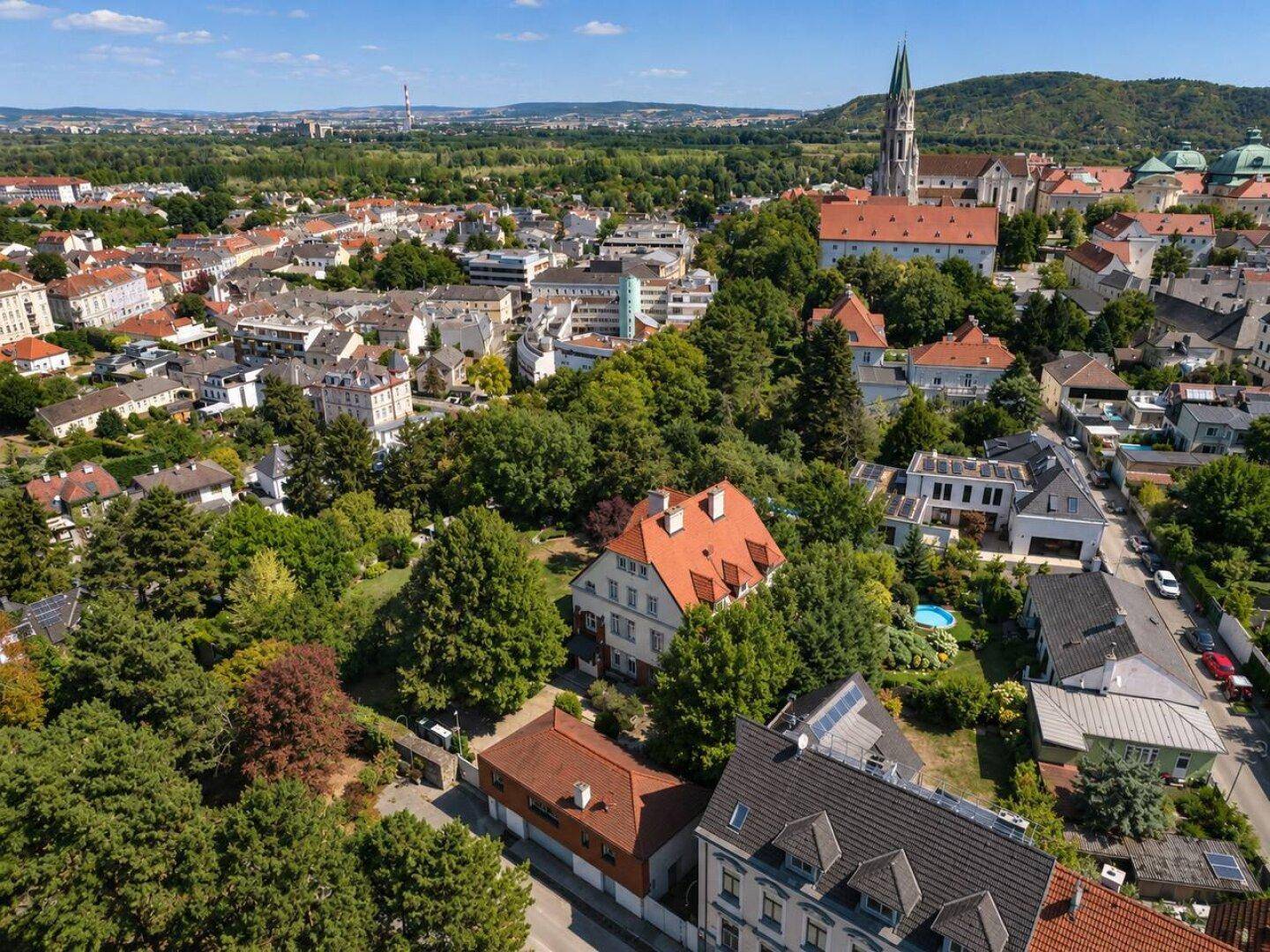 Weitläufige Luftaufnahme einer Stadt mit vielen Bäumen, Häusern und einer Kirche unter blauem Himmel.