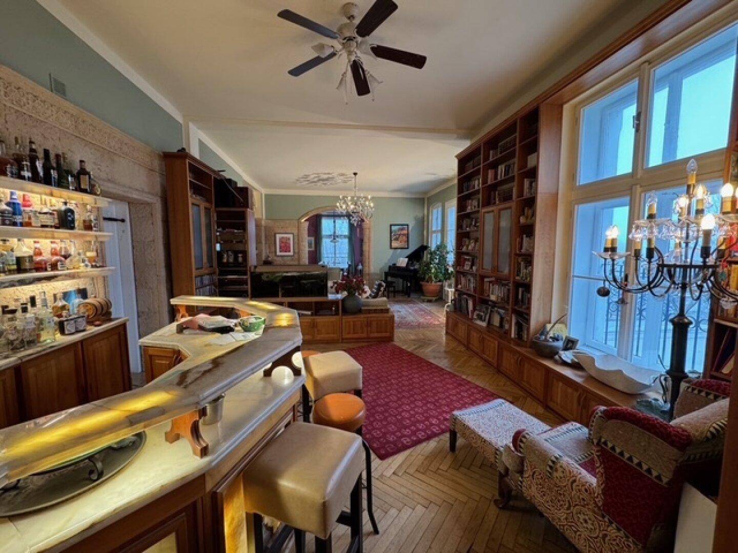 Geräumiges Wohnzimmer mit integrierter Bar, Parkettboden, hohen Fenstern und Deckenventilator.